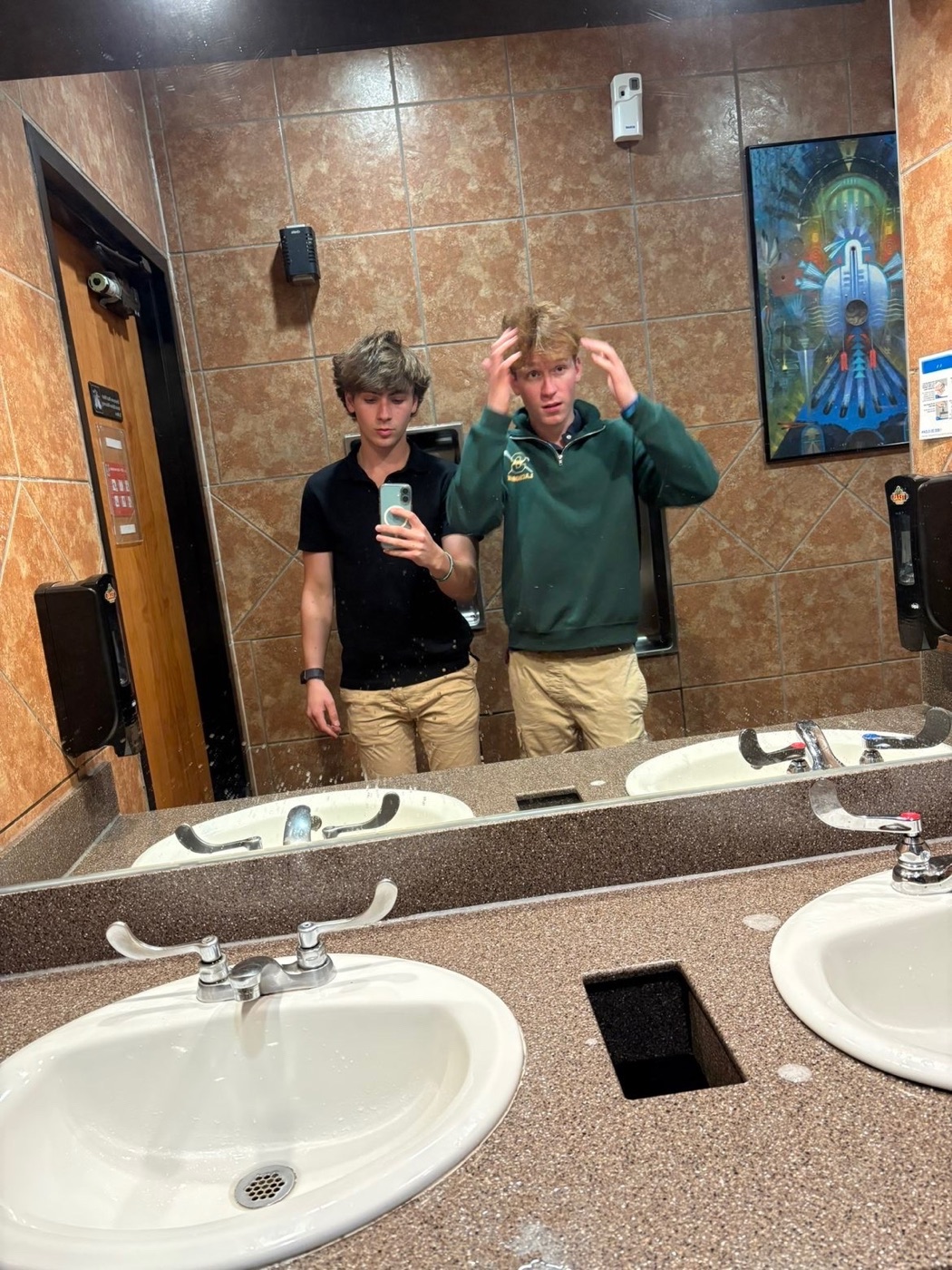 Mirror selfie of Colin and a friend in a tiled restroom